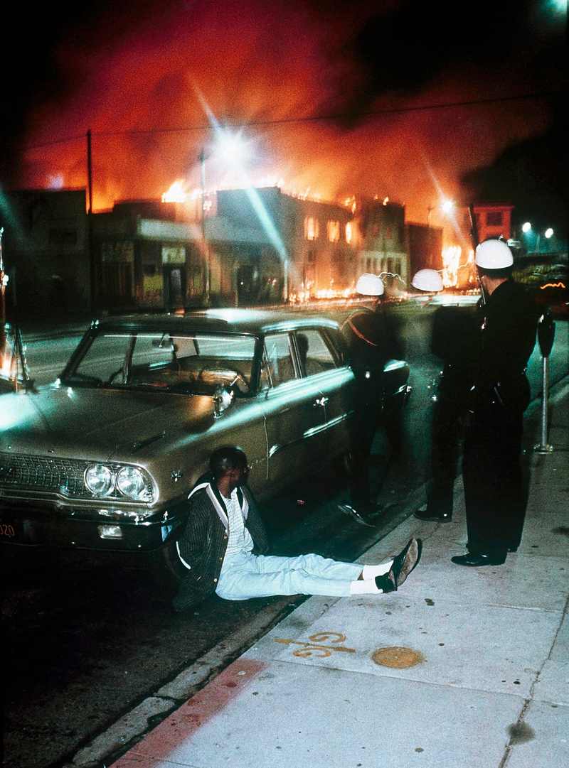 In this August 1965 file photo, police detain a man as buildings burn during rioting that swept the Watts district of Los Angeles. It began with a routine traffic stop, blossomed into a protest and escalated into the deadliest and most destructive riot Los Angeles had seen. The Watts riot broke out Aug. 11, 1965 and raged for most of a week. When the smoke cleared, 34 people were dead, more than 1,000 were injured and some 600 buildings were damaged.